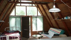 Un dormitorio acogedor en el ático, con cama, una mesita, un sofá y una ventana con cortinas.