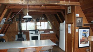 Una cocina rústica con techo de madera, estufa, refrigerador y un comedor con sillas.