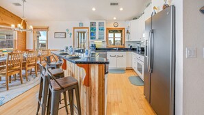 A modern kitchen with a central island, wooden bar stools, and a large refrigerator.