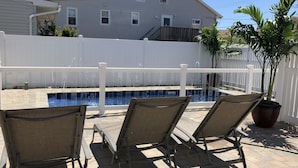 Um quintal com piscina, cerca branca e três espreguiçadeiras.