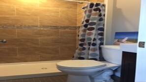 A bathroom with a shower, toilet, and a tiled wall.