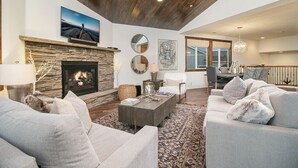 A spacious living room with a stone fireplace, comfortable seating, and a large window.