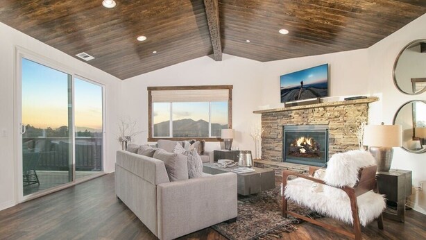 A spacious living room with a stone fireplace, a large window with a view of mountains, and a cozy seating area.