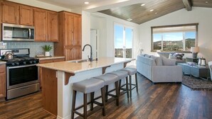 A modern kitchen with wooden cabinets, a built-in island with bar stools, a stainless steel oven, and a microwave.