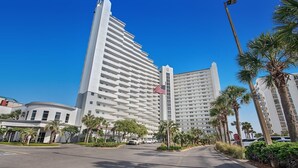 Un hôtel moderne, reconnaissable à son grand drapeau américain, entouré de palmiers et surplombant un ciel d’un bleu éclatant.