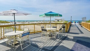 Une terrasse en bois avec des sièges et des parasols, donnant sur une plage.