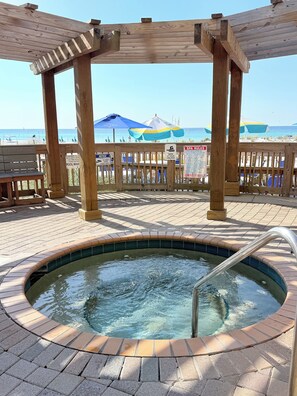 A wooden deck with a hot tub, a pool, and beach umbrellas.