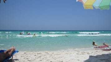Une plage à l’eau d’un bleu cristallin, où l’on peut se baigner et faire de la planche à voile, et une rive sablonneuse parsemée de chaises longues et de parasols.