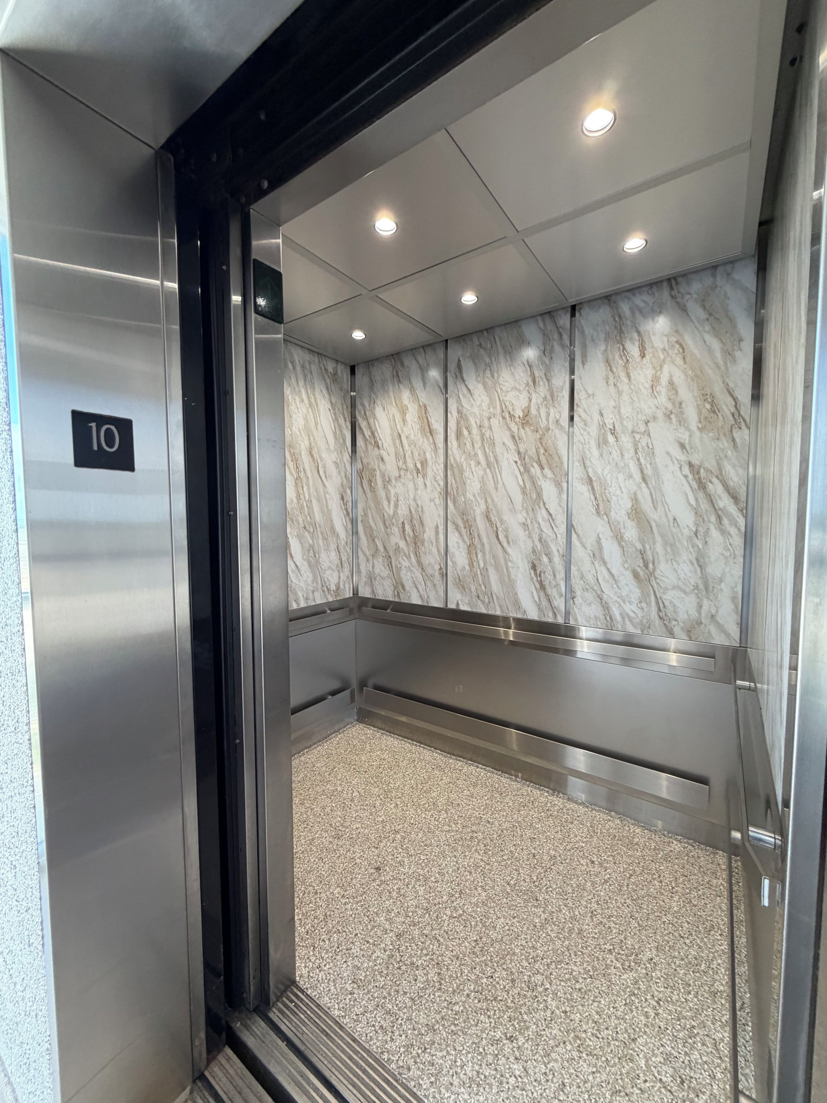 Un ascensor con pared de mármol, suelo metálico y señal con el número 10.