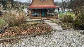 A wooden cabin with a porch, a covered entryway, and a small outdoor seating area. - KY BOURBON TRAIL LAKEFRONT HOUSE WITH DOCK SLEEPS 8! Year round Hot tub! (Lawrenceburg)