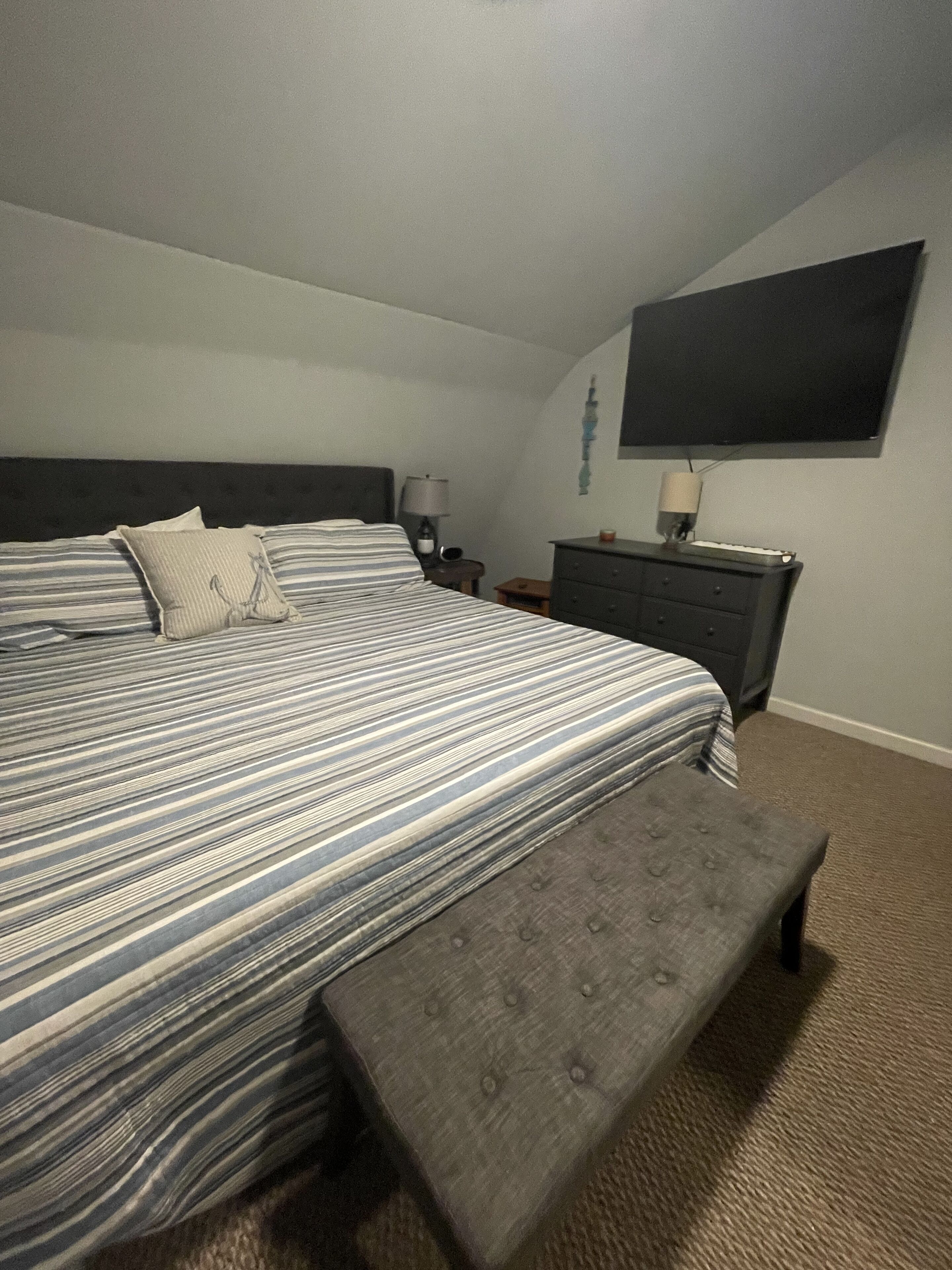 Une chambre bien rangée, avec un grand lit, des tables de chevet, une commode et un téléviseur à écran plat fixé au mur.