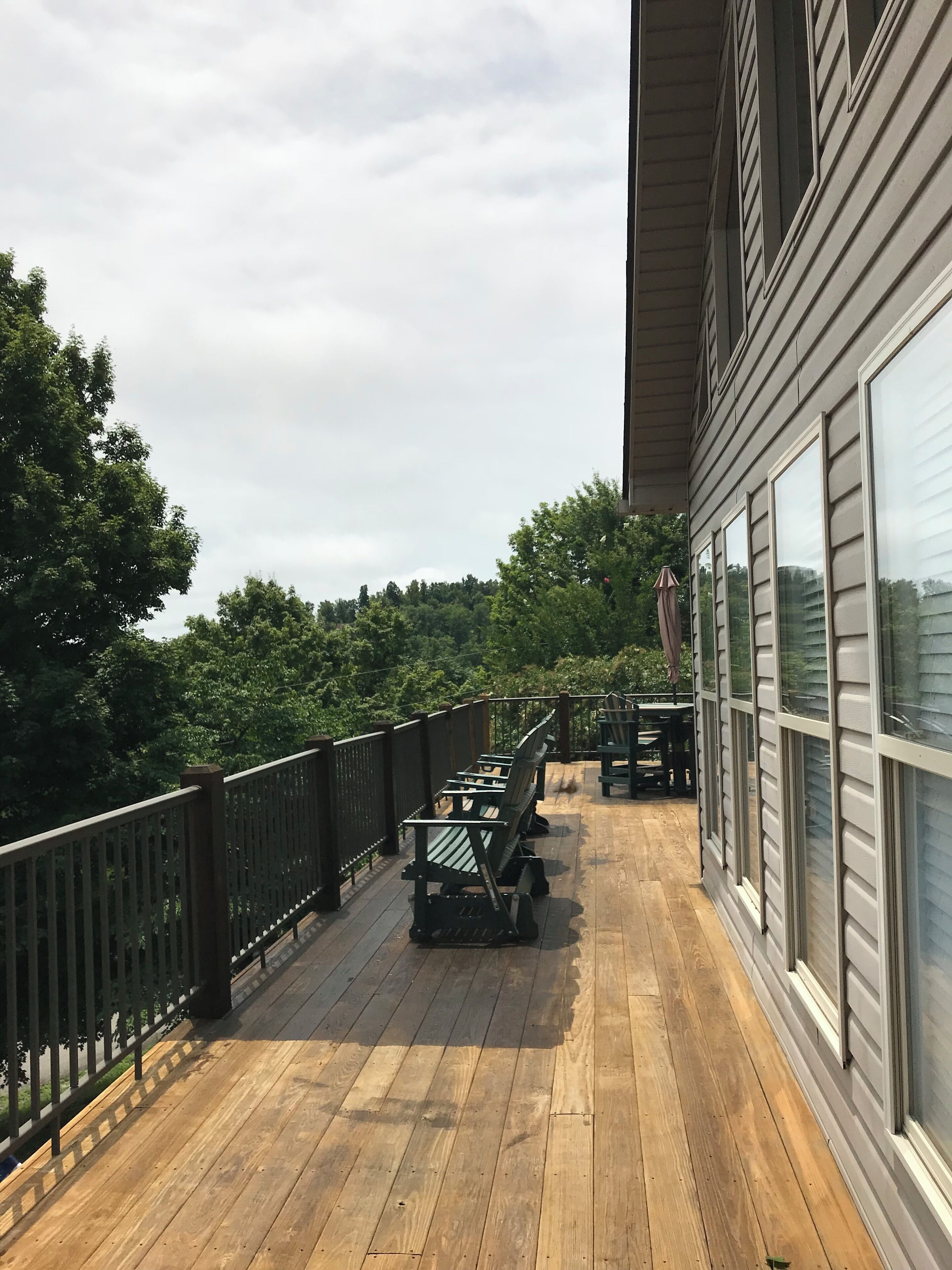 A wooden deck with outdoor furniture and a railing, overlooking a forested area.