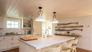 Una cocina con una isla de mármol, armarios blancos y una viga de madera rústica en la pared.