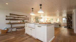 Una cocina amplia con suelo de madera, armarios blancos e iluminación colgante.