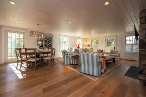 A spacious living room with a dining area, wooden floors, and large windows.