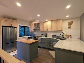 Une cuisine moderne dotée d’un îlot central, d’appareils électroménagers intégrés et offrant une vue sur les arbres à l’extérieur.
