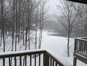 A snow-covered deck with a view of a forest and a building in the distance. - Spacious Sugarbush Retreat - Wood Stove, Outdoor Pool, Minutes to Sugarbush (Warren)