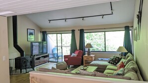 A living room with a sofa, armchair, TV, and a fireplace. - Spacious Sugarbush Retreat - Wood Stove, Outdoor Pool, 5 Mins to Sugarbush (Warren)
