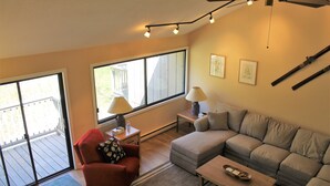 A living room with a sofa, armchair, coffee table, and two lamps. There is a ceiling fan and a window with a view of a deck. - Spacious Sugarbush Retreat - Wood Stove, Outdoor Pool, 5 Mins to Sugarbush (Warren)