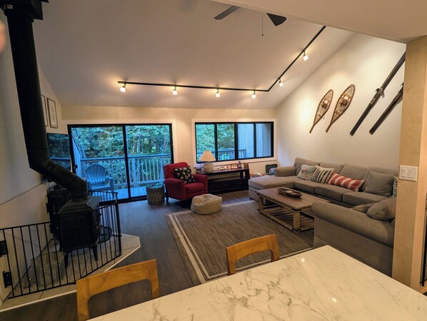 A modern living room with a fireplace, a sofa, a dining table, and large windows.