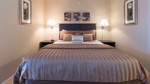 Une chambre à coucher bien rangée, avec un grand lit, deux tables de chevet et trois tableaux encadrés accrochés au mur.