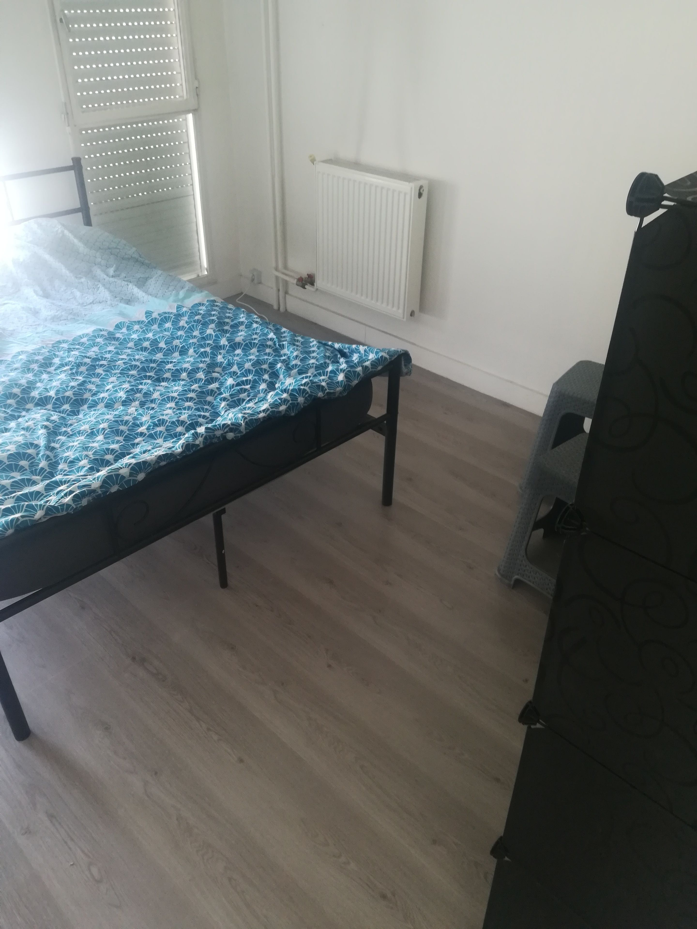 A room with a bed, a radiator, and a window with blinds.