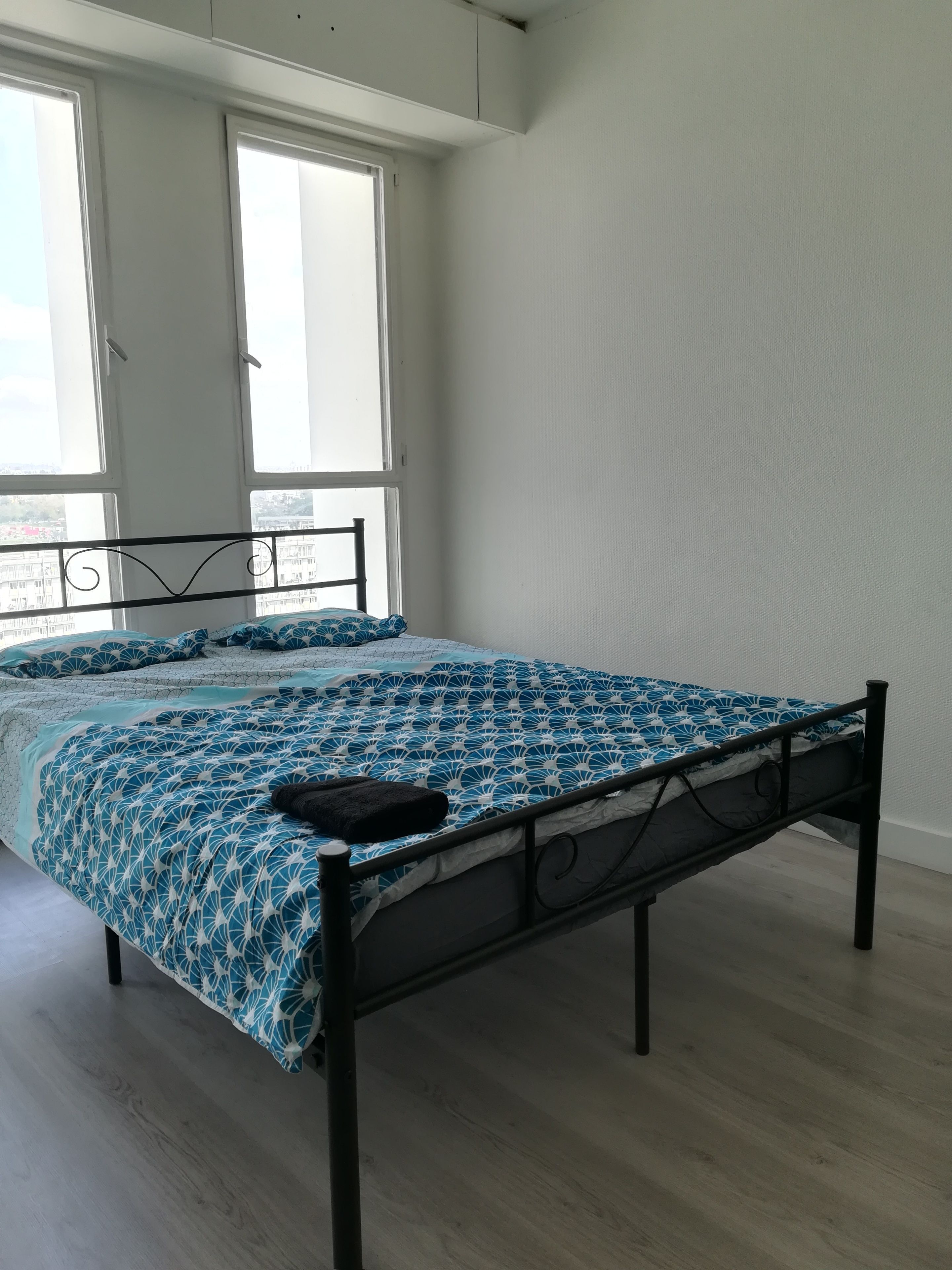 Een slaapkamer met een bed, grote ramen en uitzicht op gebouwen.