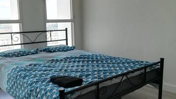 Een slaapkamer met een bed, grote ramen en uitzicht op gebouwen.