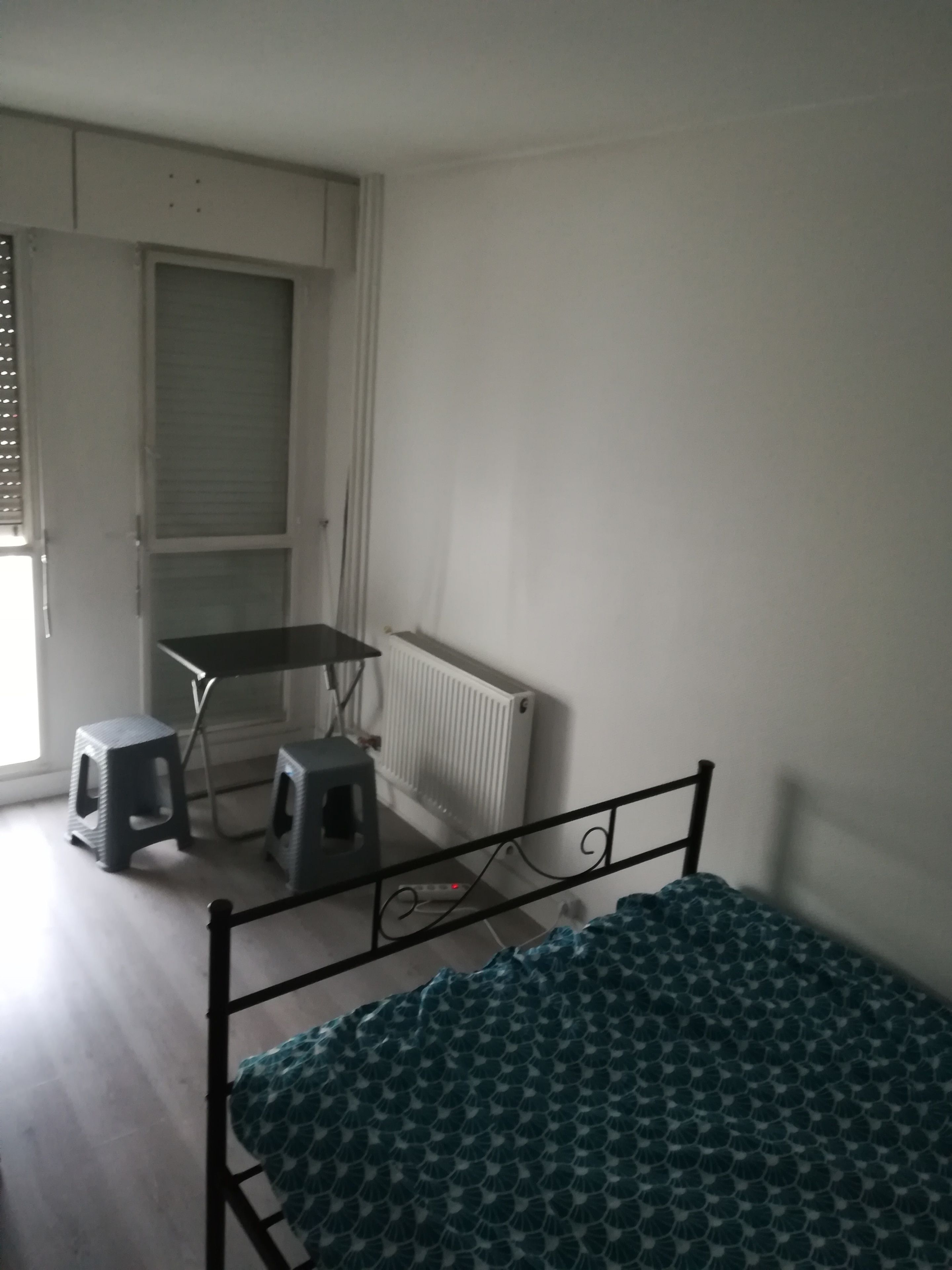 Una habitación con cama, un radiador, un escritorio y dos taburetes.