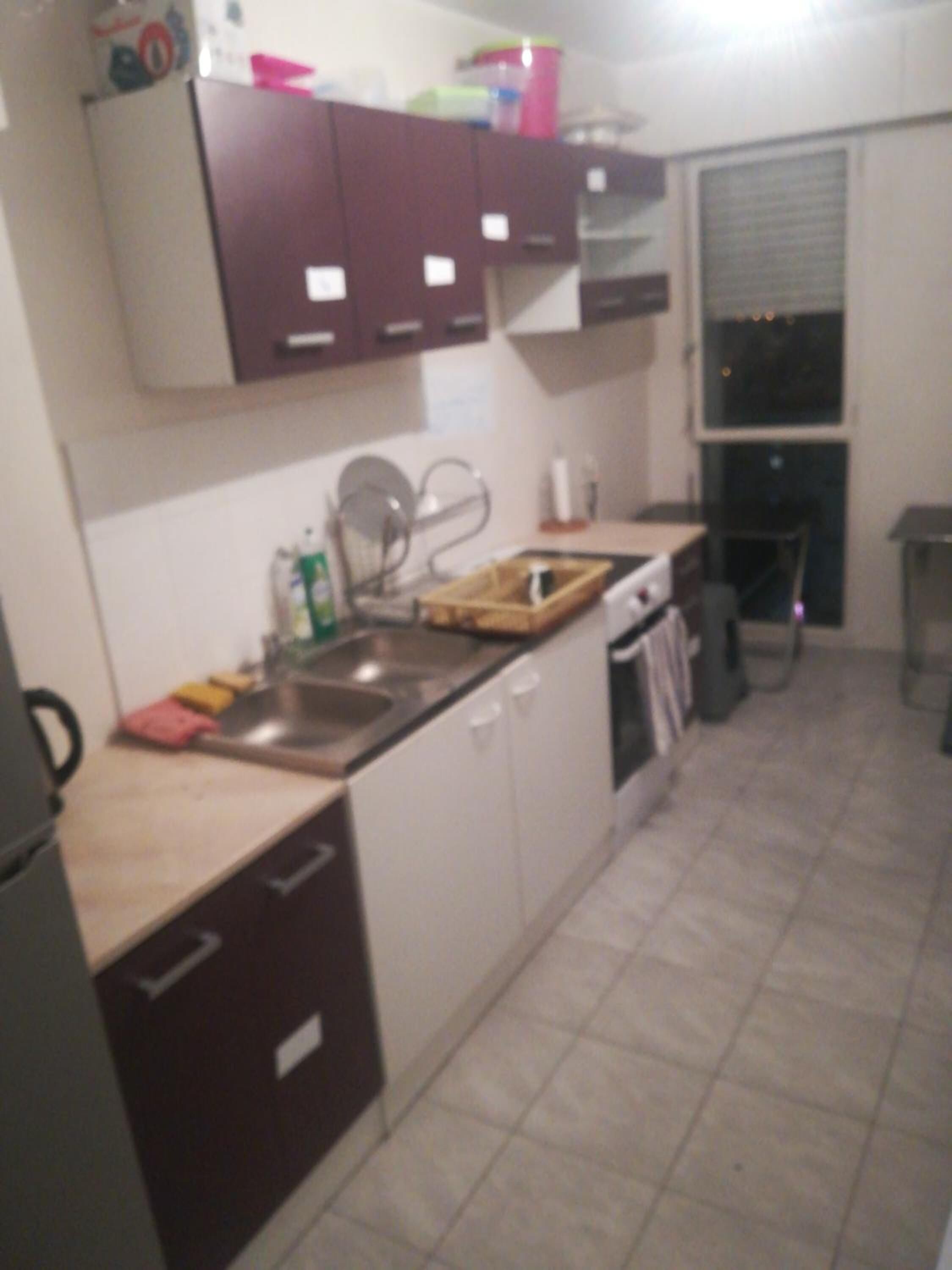 Una cucina con mobili bianchi, un lavello in acciaio inossidabile e una finestra con persiane.