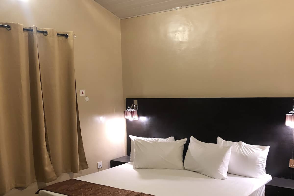 Un lit bien fait, avec du linge de lit blanc et marron, une tête de lit sombre et une table de chevet avec une lampe.