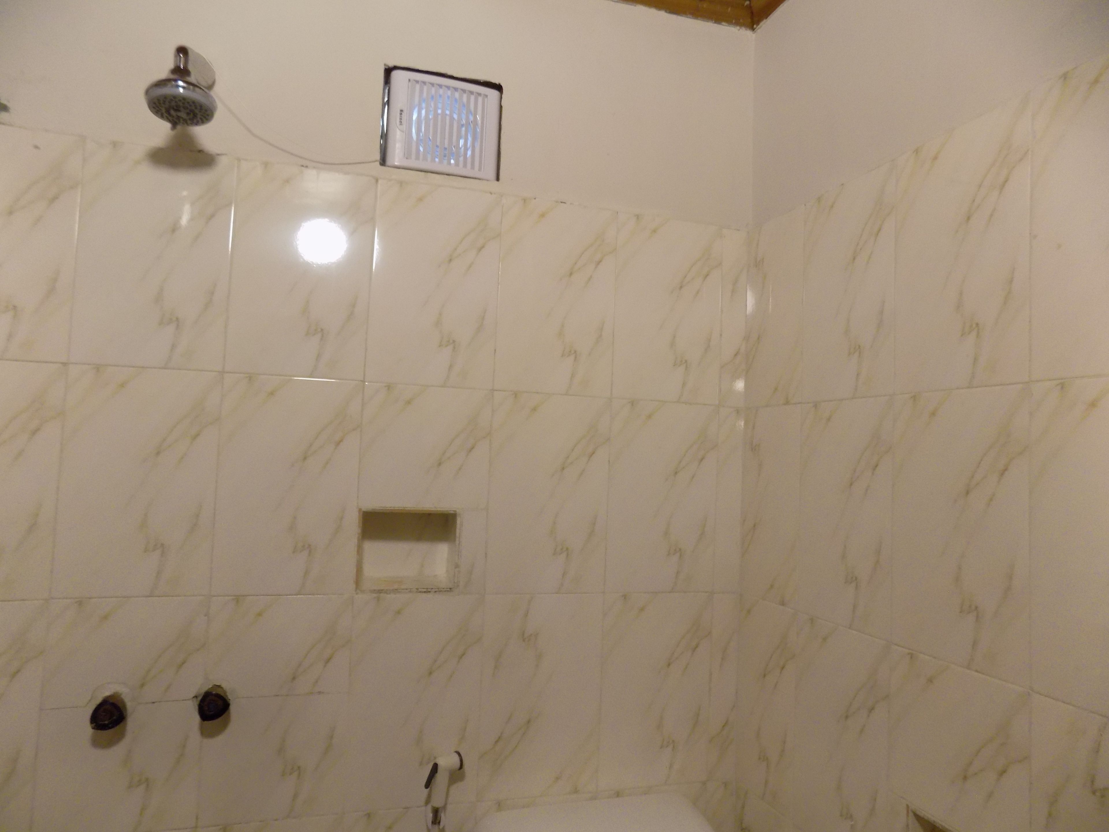A bathroom with marble tiles, a shower, and a small window.