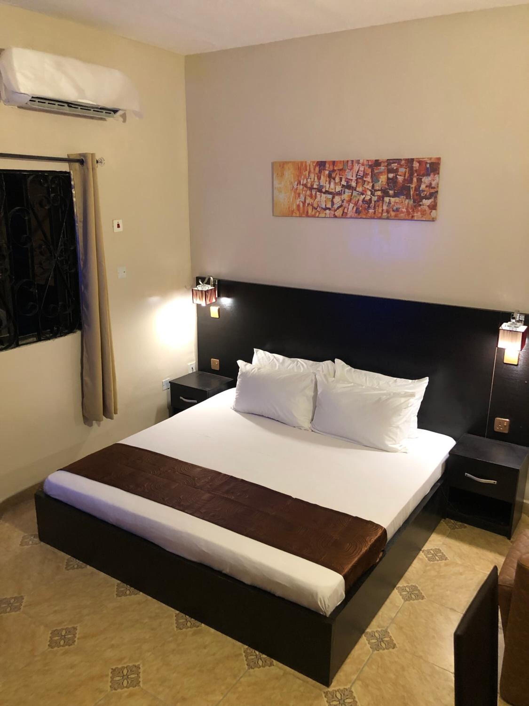 A neatly made bed with white and brown linens, a black headboard, and two bedside tables with lamps.