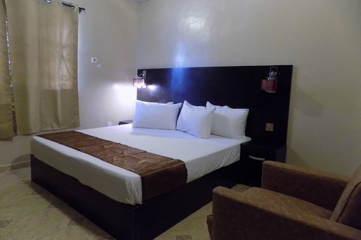Une chambre d’hôtel avec un grand lit, une table de chevet, une chaise et un rideau.