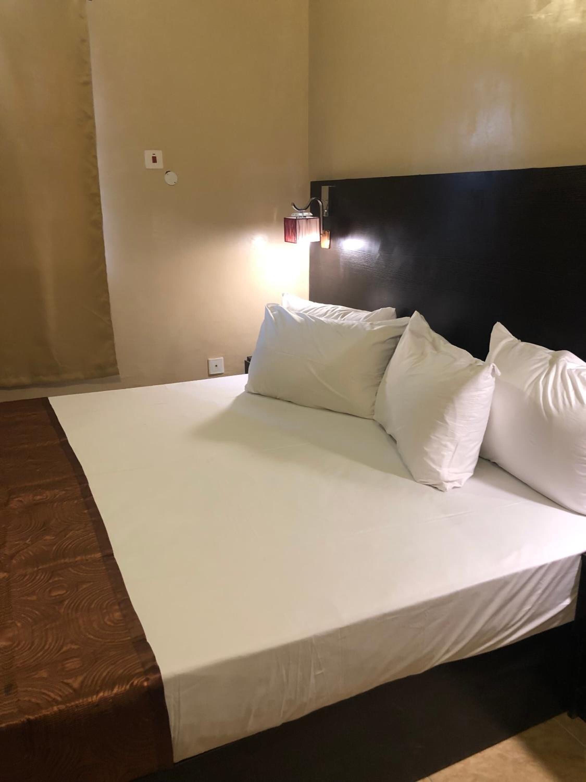 A hotel room with a large bed, a headboard, and a wall-mounted light fixture.