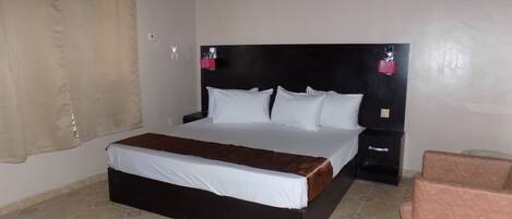 Una habitación de hotel con una cama grande, una mesita de noche, una silla y una cortina.