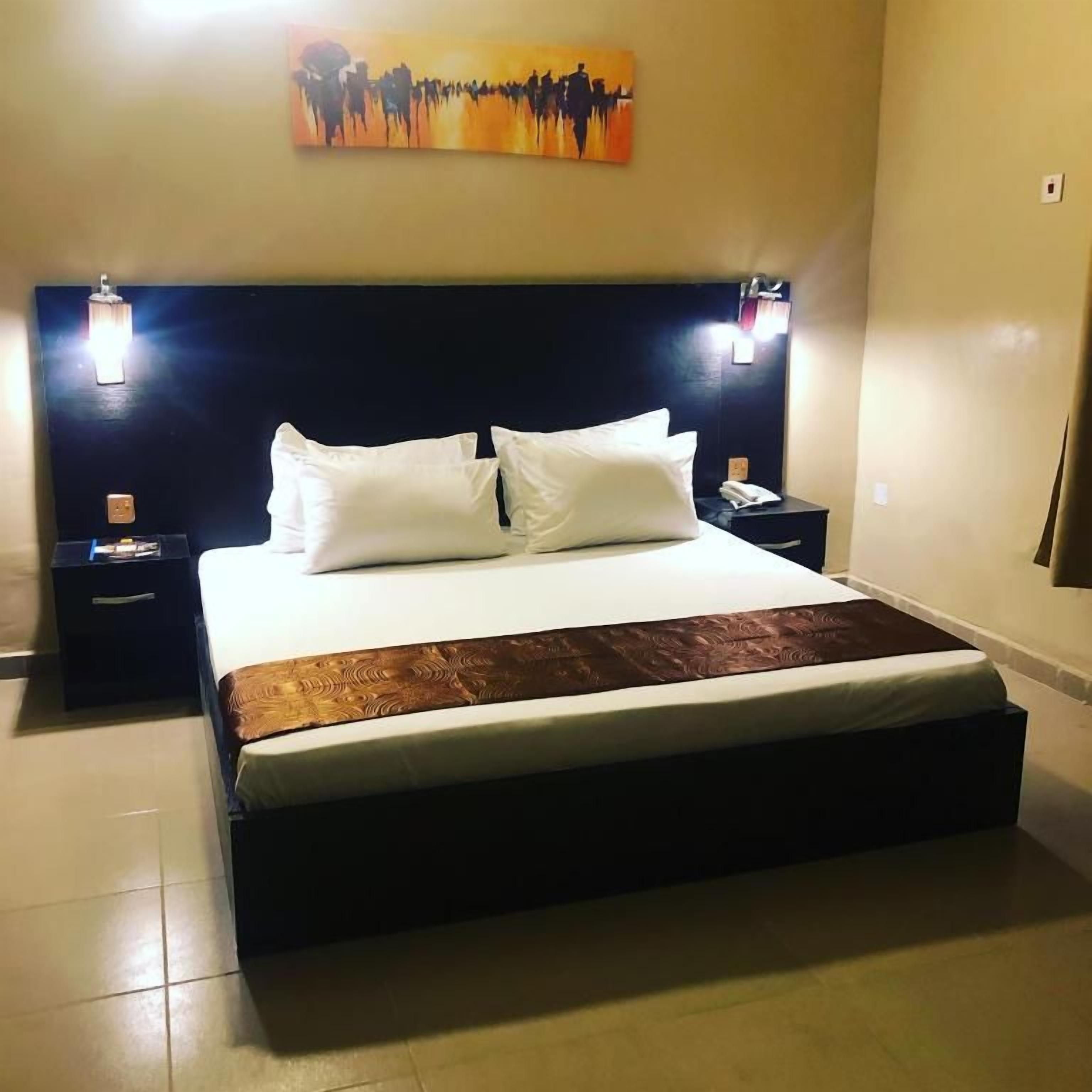 A hotel room with a large bed, two bedside tables, a wall-mounted artwork, and a nightstand with a lamp.