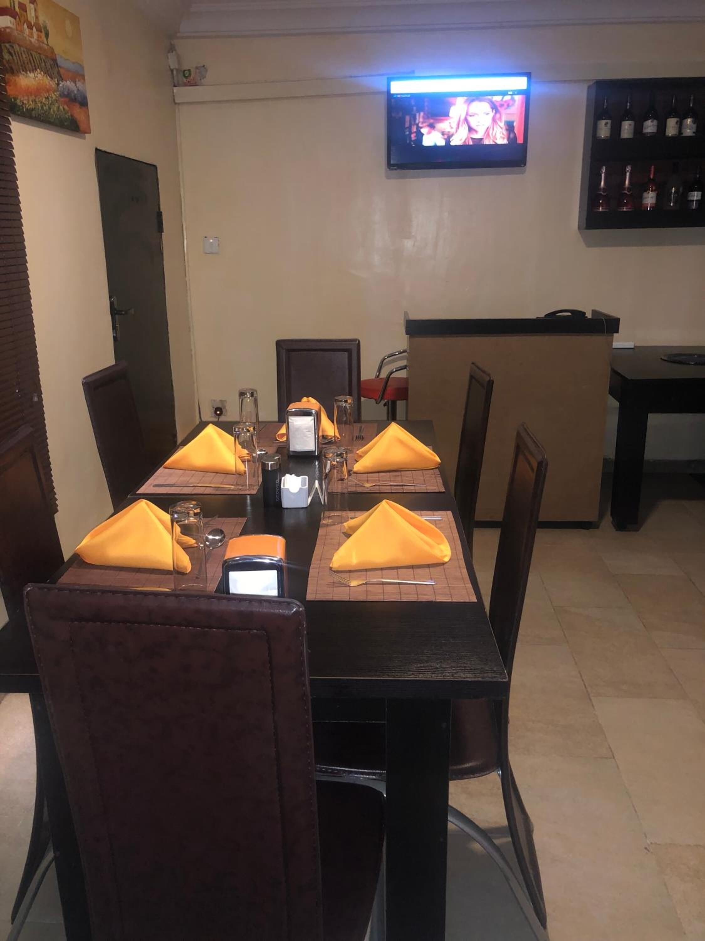 A dining area with a table set for four, a television mounted on the wall, and a bar with bottles.