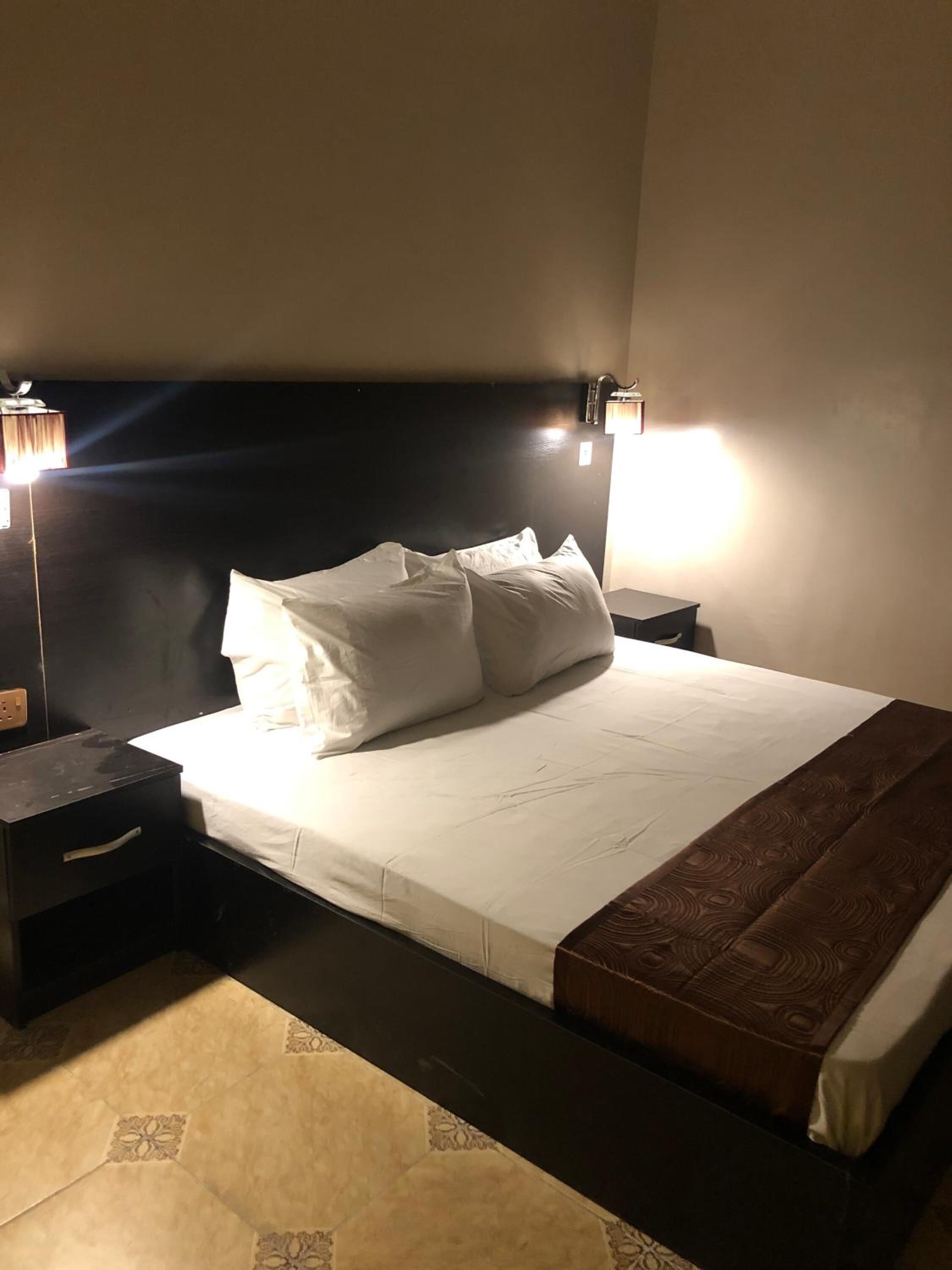 A neatly made bed with white linens and a brown throw blanket, flanked by two bedside tables with lamps.