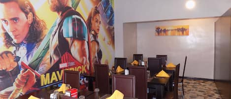 Restaurante com mesas postas para refeições, um cartaz de cinema grande na parede e um quadro na parede.