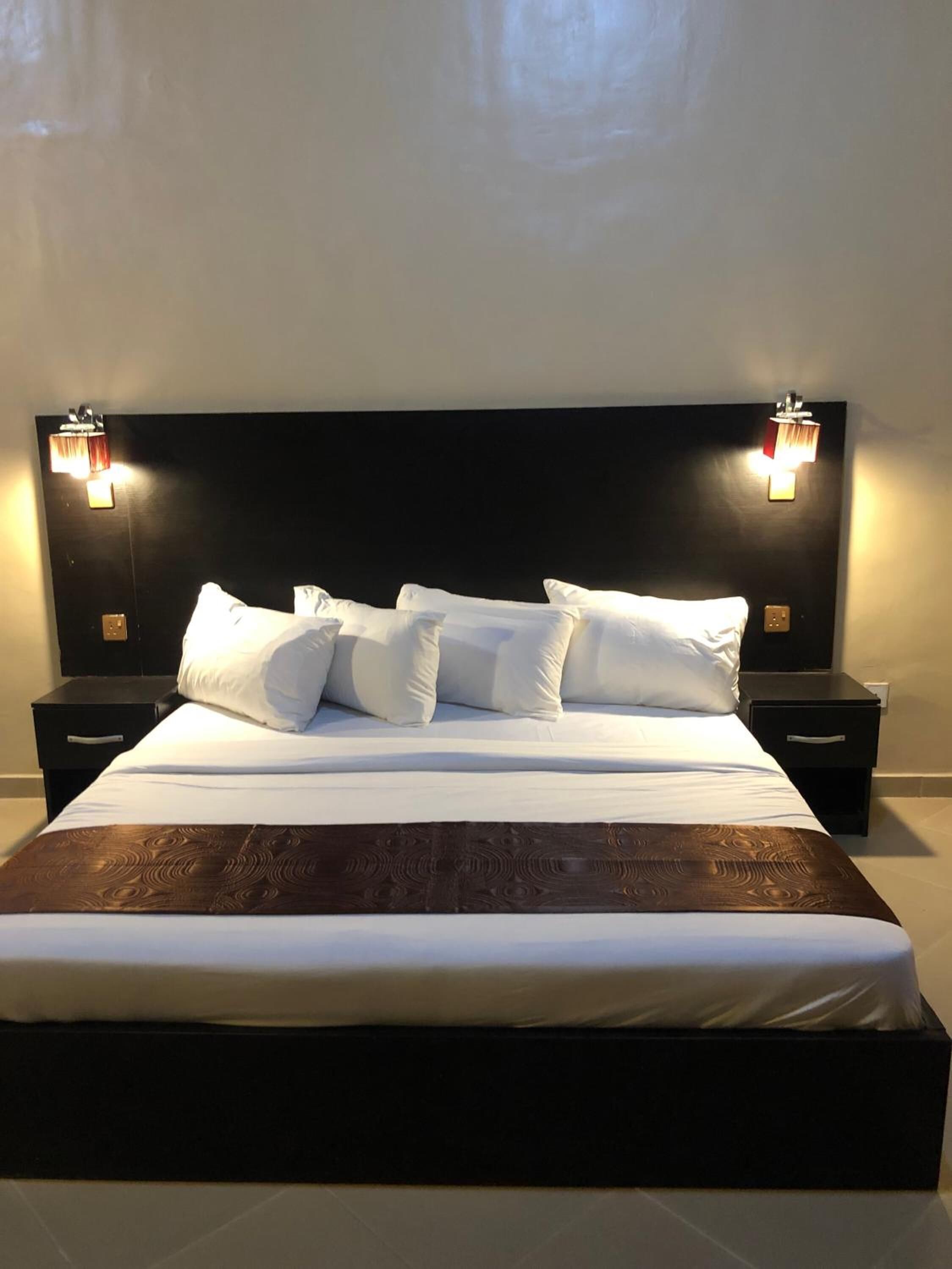 A neatly made bed with white linens and a dark wooden headboard. There are two bedside tables with lamps on either side of the bed.