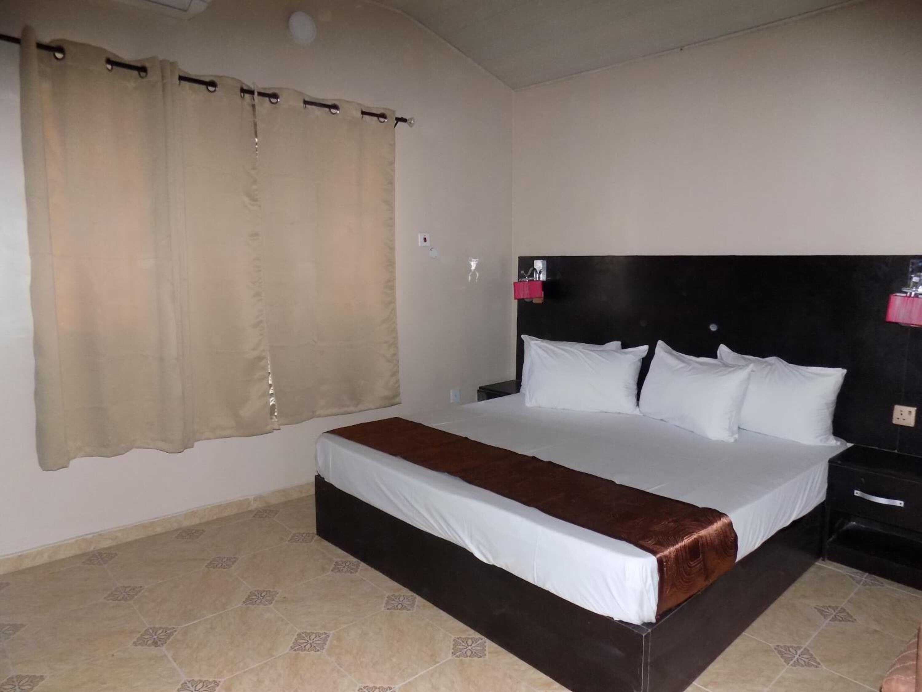 A hotel room with a large bed, a nightstand, a headboard, and a curtain.