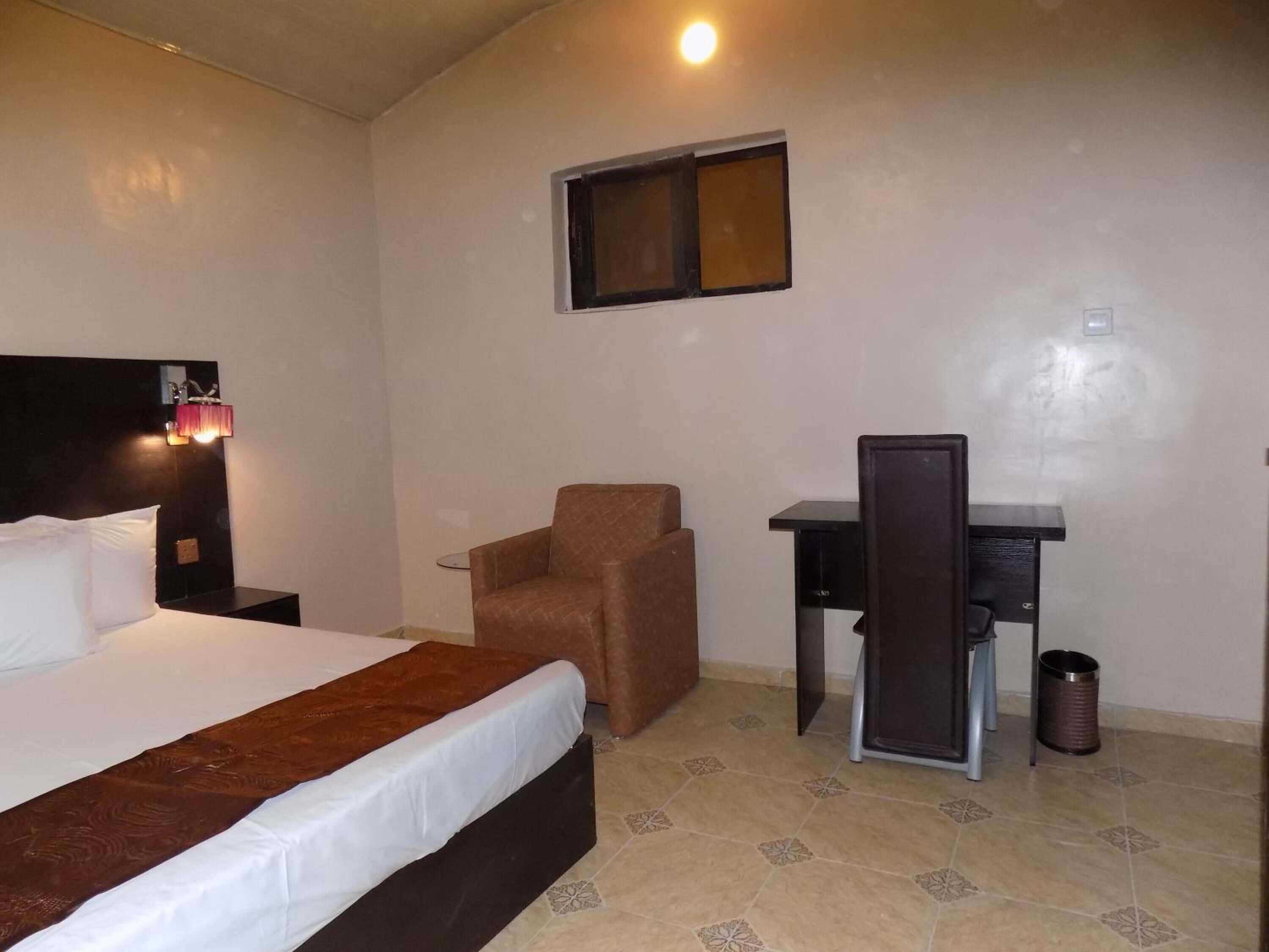 A hotel room with a bed, a desk, a chair, and a trash bin.
