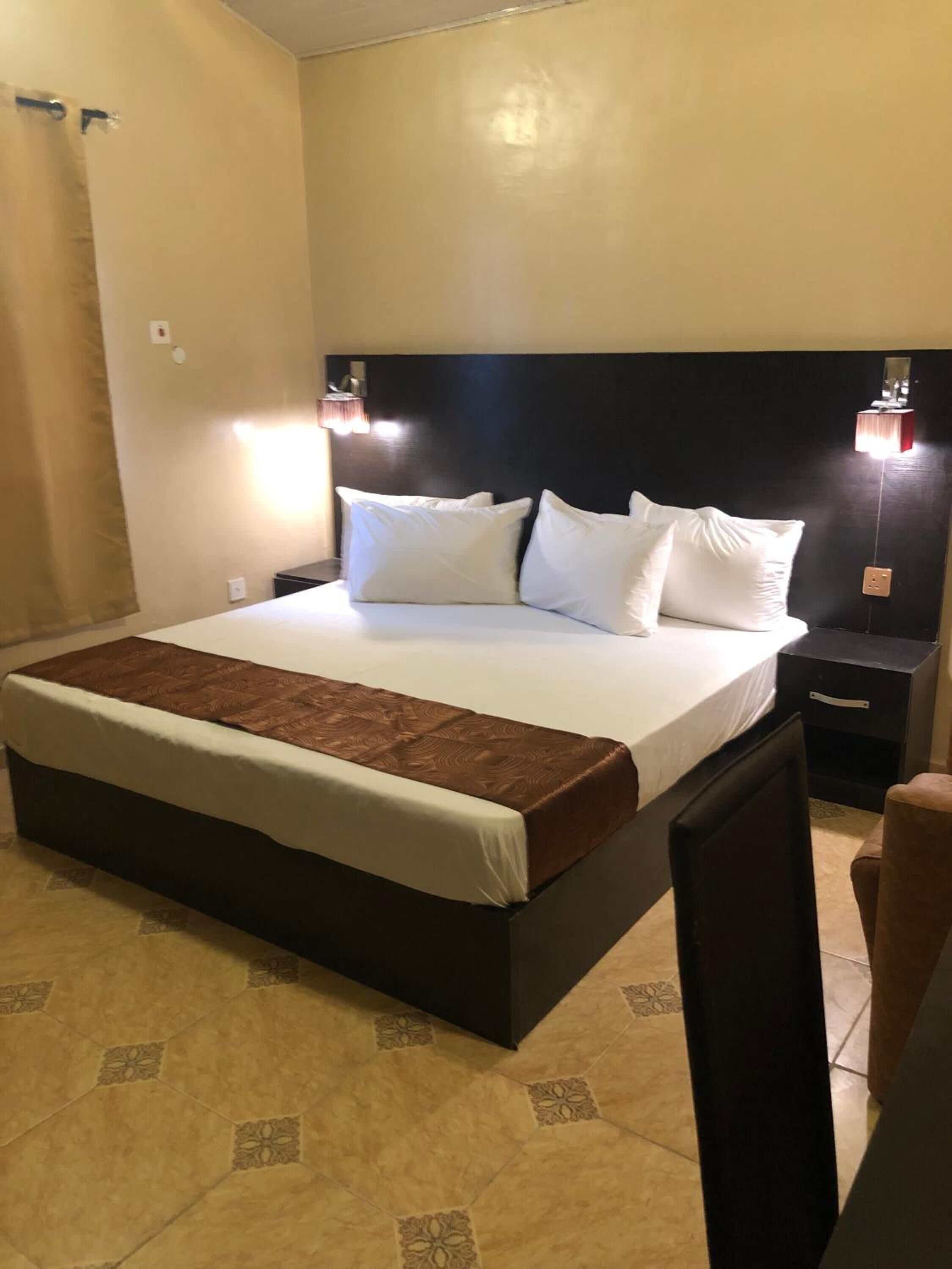 A hotel room with a large bed, two bedside tables, a nightstand, and a chair.