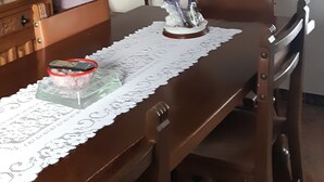 A dining table with a lace tablecloth, a wooden chair, a small statue, and a decorative fan on the wall.