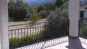 A balcony with a view of a mountainous landscape, a stone floor, and a metal railing.