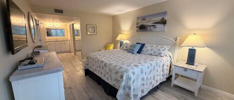 Un dormitorio con cama, mesitas de noche, cómoda, espejo y un cuadro en la pared.