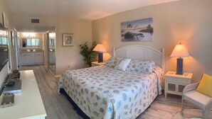 A bedroom with a bed, bedside lamps, a chair, a desk, and a view of the bathroom. - Siesta Dunes 5-303, Come enjoy our little piece of Paradise! (Siesta Key)