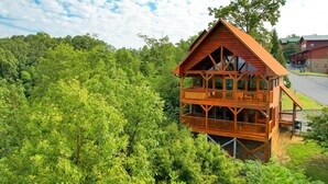 A wooden cabin with a balcony, surrounded by dense forest. - 🌙 Midnight Wonder 🏔️ Twinkling Valley Lights, Hot Tub & Resort Pool (Sevierville)