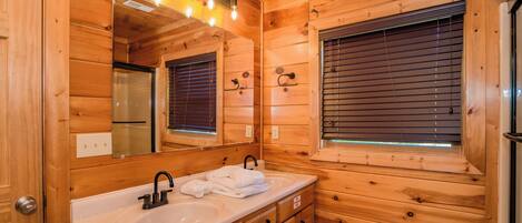 A wooden cabin bathroom with a double sink, a mirror, and a window with blinds.